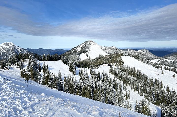 Verschneite Berglandschaft unter blauem Himmel, mit dichten Nadelwäldern und sanften Hügeln. Eine klare Winteridylle mit weitem Blick in die Ferne.