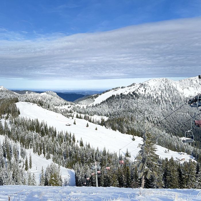 Schneebedeckte Berge mit Skiliften und bewaldeten Hängen unter einem teils bewölkten blauen Himmel. Die Landschaft bietet eine idyllische Winterkulisse.