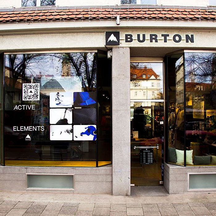 Außenansicht eines modernen Geschäfts mit großen Glasfenstern. "BURTON" steht über dem Eingang. Im Inneren sind Bekleidungs- und Sportartikel sichtbar.