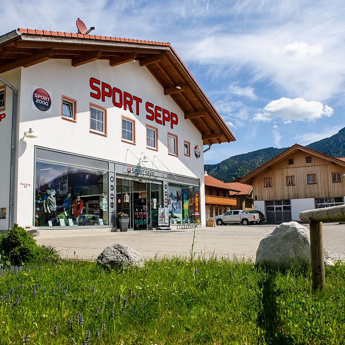 Ein Sportgeschäft mit der Aufschrift "Sport Sepp" vor einer malerischen Berglandschaft. Der Laden hat weiße Wände und ein rotes Dach.