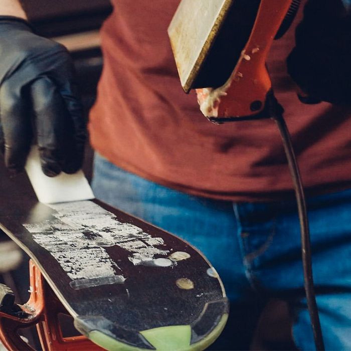 Person trägt Skihandschuhe und schleift eine Skiunterseite mit einer Maschine. Der Ski ist in einer Werkstattklemme befestigt.