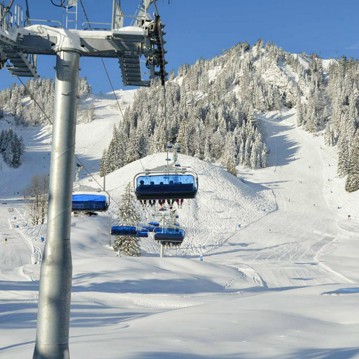 Snowy ski resort with chairlifts, snow-covered mountains, and skiers under a clear blue sky.