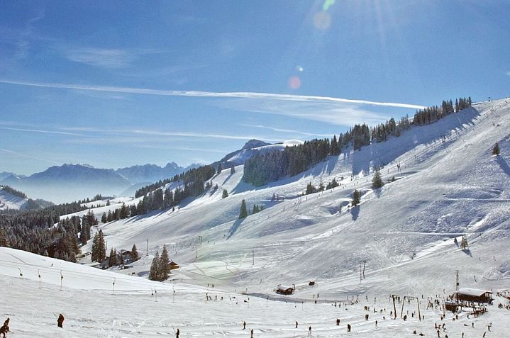Schneebedeckte Berglandschaft mit Skilift, blauen Himmel und Sonnenschein. Skifahrer genießen die Pisten, während Bäume die Winterkulisse ergänzen.