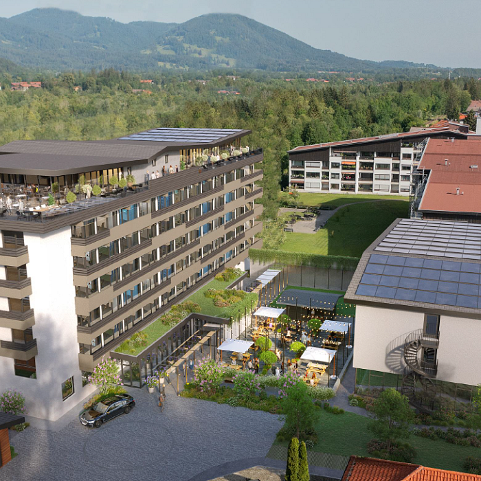 Luftaufnahme eines modernen Hotelkomplexes mit mehreren Gebäuden, umgeben von grüner Landschaft und Bergen im Hintergrund, bei sonnigem Wetter.